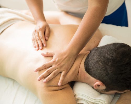 Closeup of a young man and a therapist's hands giving a back massage in a spa clinic